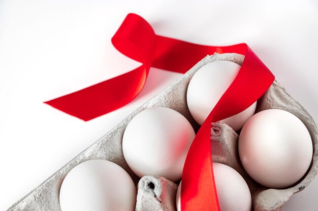 Easter eggs in a cardboard box with a red festive ribbon on a white background