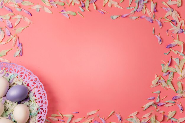 Easter eggs and colorful petals of spring flowers on a light pink warm background.