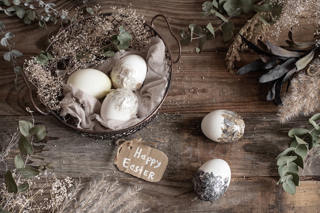 Uova di pasqua in un cesto decorativo con fiori secchi su un tavolo di legno. felice pasqua concetto.