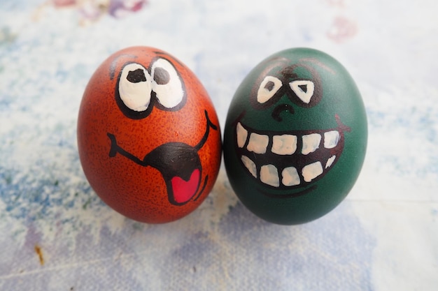 Easter eggs dyed green and brown with painted laughing faces Funny grimaces with eyes tongue and big white teeth Scary face for Halloween Emoticon for Easter Light abstract background