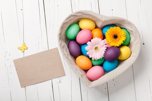 Easter eggs and gerbera flowers in heart shaped basket