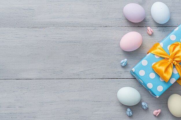 Easter eggs and gift box with beautiful bow on wooden gray background