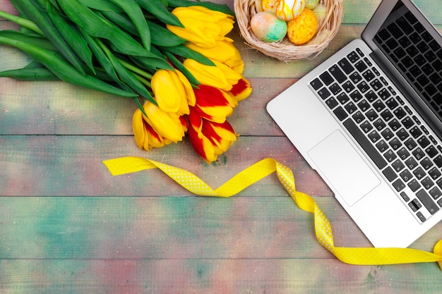 Easter eggs, laptop and bouquet of tulips.