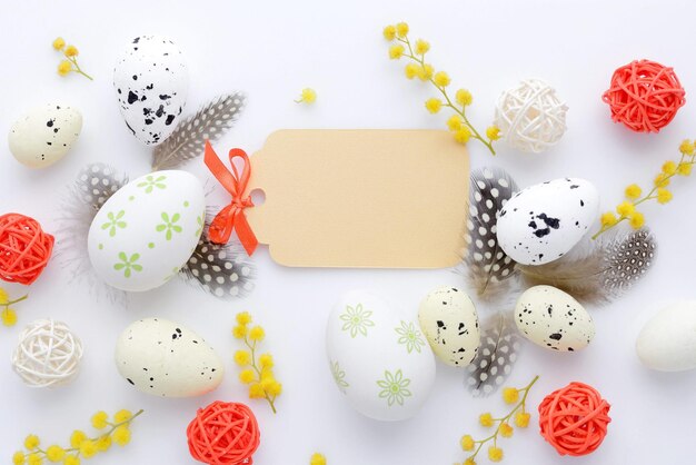 Easter eggs and mimosa flowers on white background with blank card to greet top view
