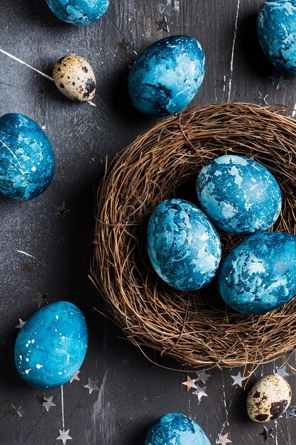 Photo easter eggs in nest painted by hand in blue color on dark background