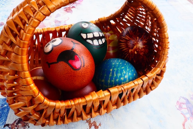 Easter eggs painted in different colors with painted laughing faces Funny grimaces with eyes tongue and big white teeth Scary face for Halloween Emoticon for Easter Wicker basket White background