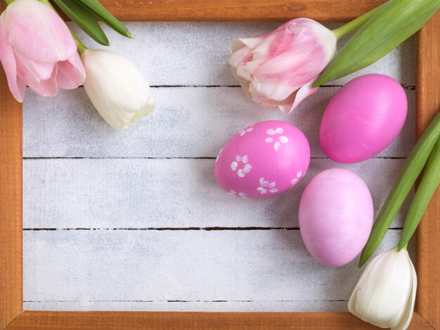 Easter eggs, photo frame, tulips on a white wooden background.