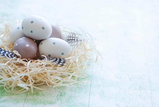 Пасхальные яйца в соломенном гнезде на зеленом деревянном фоне