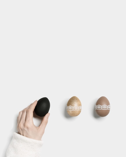 Tendenza delle uova di pasqua colore oro nero e beige su sfondo bianco simbolo della stretta della mano della donna