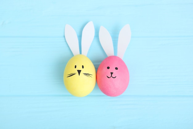 Easter eggs with cute faces and ears on a colored background