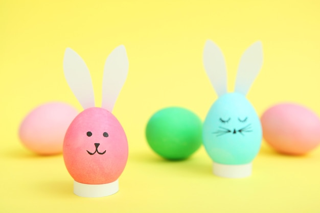 Easter eggs with cute faces and ears on a colored background