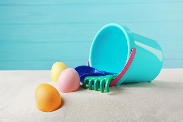 Easter eggs with sand and pail on wooden blue background