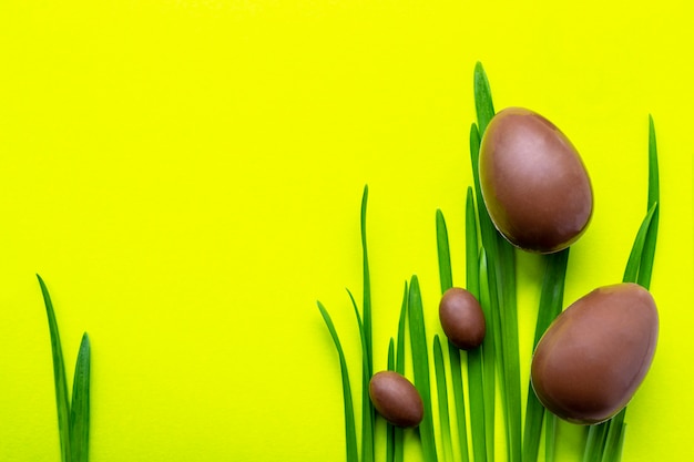 黄色の背景にイースターエッグ。緑の芝生に2つの大きなチョコレートの卵と2つの小さなチョコレートの卵。イースター休暇のコンセプトと楽しい。テキストのための場所。