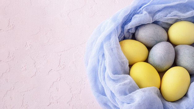 Le uova di pasqua nei colori pastello gialli e blu nel nido blu del tessuto su fondo rosa con lo spazio della copia