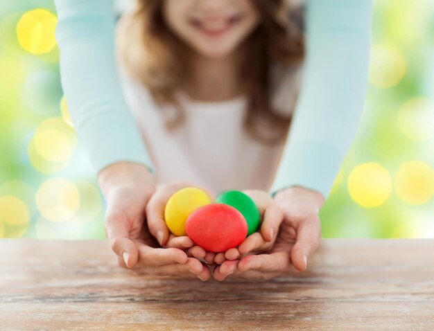 easter, family, people, holiday and childhood concept - close up of happy girl and mother hands holding colored eggs over green lights background