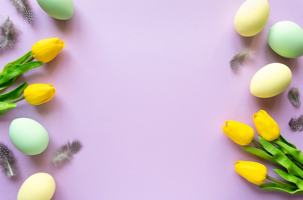 Easter flat lay. Painted eggs with tulips and feathers on lilac background, copy space