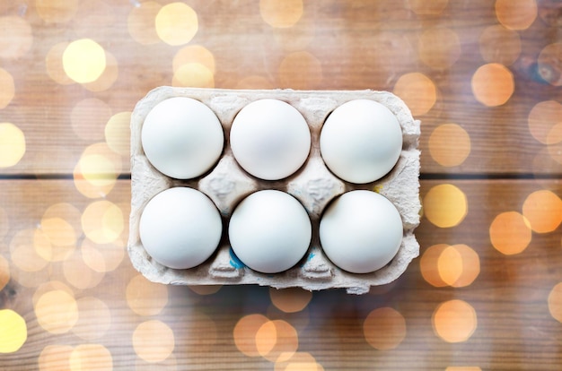 easter, food, cooking and object concept - close up of white eggs in egg box or carton wooden surface