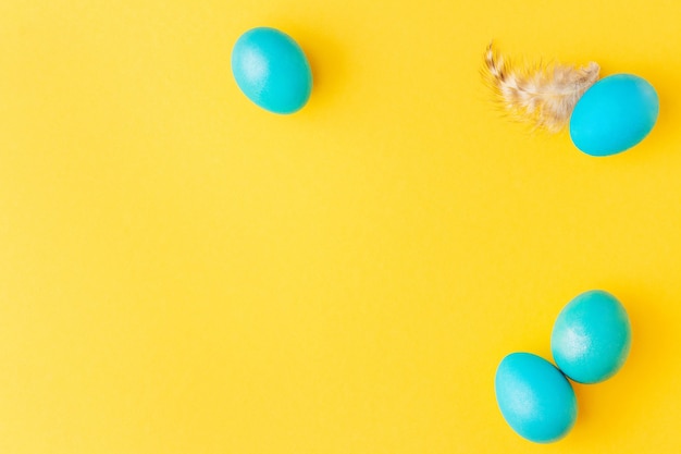 Easter frame made of blue eggs and feather on yellow background