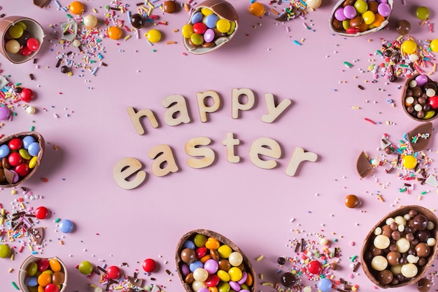 Easter frame with chocolate eggs and sweets on a pink background. Happy easter text. Top view, flat lay