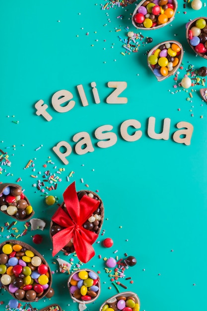 Easter frame with chocolate eggs and sweets on a turquoise green blue background Feliz Pascua  happy easter text in Spanish Top view flat lay