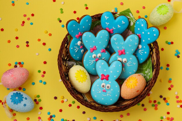 Easter funny rabbits, homemade painted gingerbread biscuits in glaze on a yellow surface, Top view