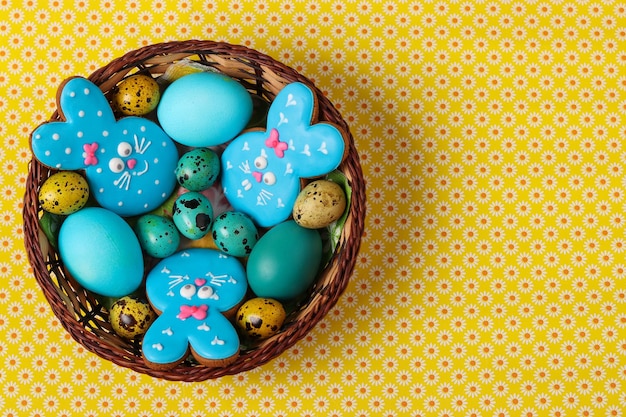 Easter gingerbreads rabbits  yellow and blue chicken and quail eggs in a wicker basket top view