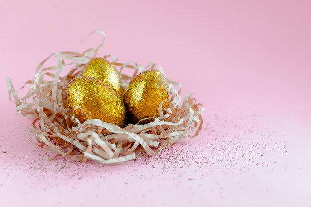 Easter golden decorated eggs in nest on pink background . Minimal easter concept copy space for text.