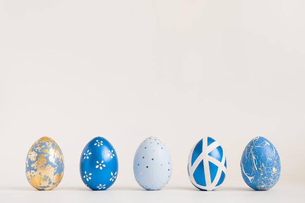 Easter golden decorated eggs stand in a row on blue surface. Minimal easter concept. 