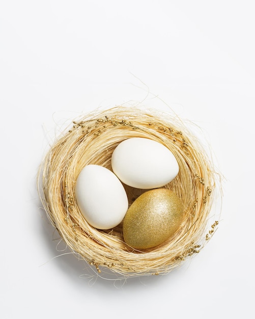 白い背景の上のわらの巣のイースター黄金の卵春の休日のためのトレンディな金の卵