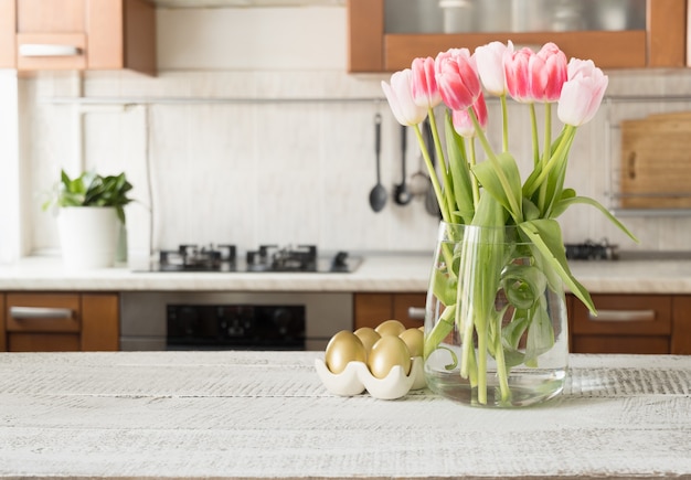 Easter golden painted eggs and spring bouquet in kitchen. Indoors.