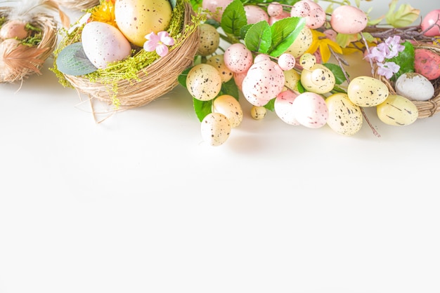 Easter greeting card background. Spring tree decor branches with colorful eggs, flowers and leaves on white background copy space for your text