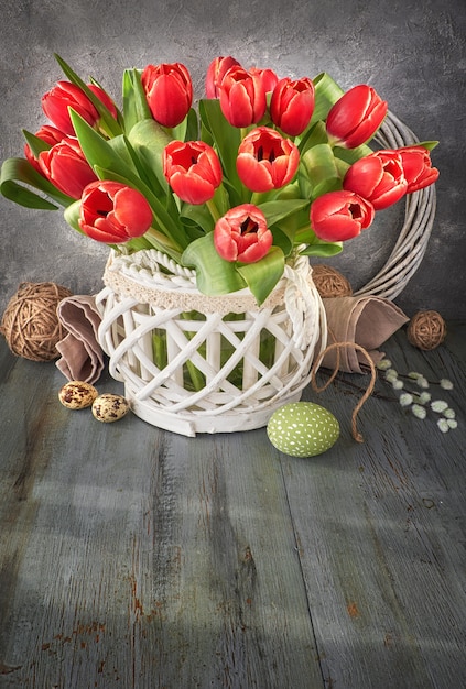 Easter greeting card design with bunch of red tulips on rustic wall with Easter decorations, text space