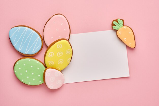 Easter greeting card with colorful rabbits, eggs, chickens and carrots gingerbread cookies on pink background with copy space. Top view.