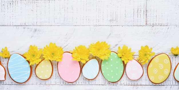 Easter greeting card with colorful rabbits, eggs, chickens and carrots gingerbread cookies on white wooden old background with copy space. Mock up. Banner. Top view.