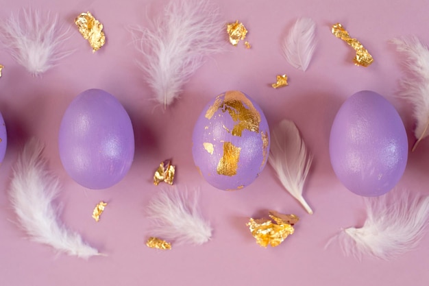 Easter greeting card with violet eggs with golden foil white feathers on violet background