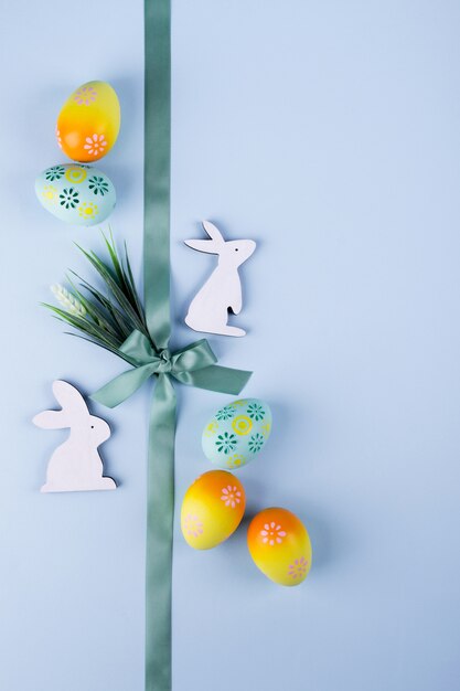 Easter holiday background with colorful painted chicken eggs decorative wooden bunny and flowers and ribbon. Flat lay