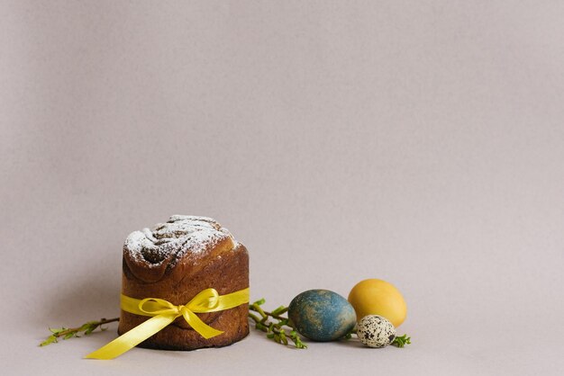 Foto cartella delle vacanze di pasqua torta dolce con zucchero in polvere e quaglie e uova di pollo colorate su uno sfondo beige chiaro con rami verdi