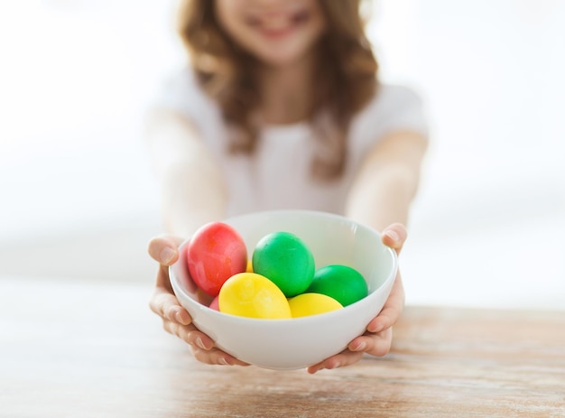 easter, holiday and child concept - close up of little girl holding bowl with colored eggs