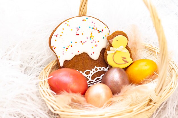 Easter holiday Colored eggs in a basket Easter gingerbread chicken and Easter cake on a light background