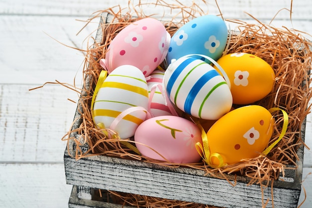 Easter holiday Colorful Easter eggs in wooden basket on white wooden background Easter greeting card Top view copy space