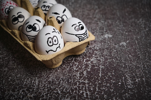 마스크에 부활절 휴가 달걀. 코로나 바이러스 전염병 기간 동안 부활절 휴가에 의료 마스크를 쓰고 그려진 재미있는 얼굴로 흰 계란 트레이를 닫습니다.