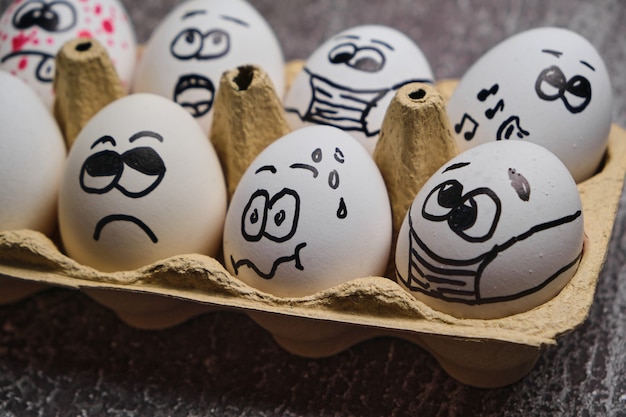 Easter holiday eggs in masks. Tray of white eggs with drawn funny faces wearing medical masks at Easter holiday during coronavirus epidemy close up