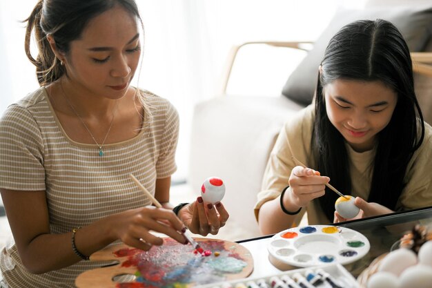 easter holiday and fun time two asian sisters painting and drawing an easter egg together