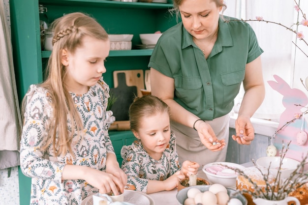 Foto tempo di vacanze di pasqua nella stagione primaverile famiglia felice candida bambini piccoli sorelle ragazze insieme madre si divertono a casa a decorare la tavola per il pranzo o la cena cibo tradizionale decorazioni per la casa festiva