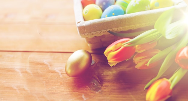 Foto pasqua, vacanze, tradizione e concetto di oggetto - primo piano di uova di pasqua colorate nel cesto e fiori di tulipano