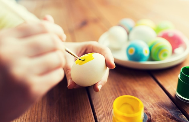 easter, holidays, tradition and people concept - close up of woman hands coloring easter eggs with colors and brush