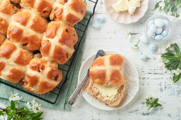 Easter hot cross buns traditional easter treats cross buns with raisins butter chocolate candy eggs with blossoming cherry or apple flowers on rustic light wooden backgrounds easter holiday meal