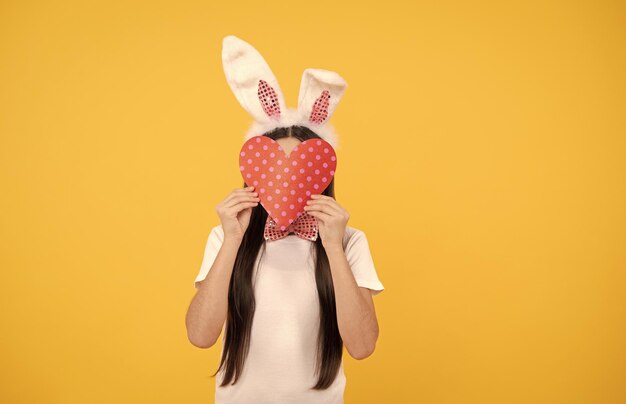 Пасхальная девочка в кроличьих ушах и галстуке-бабочке держит сердце любви счастливого пасхального веселья