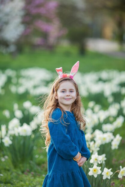 Easter Little cute girl 5 years old with rabbit ears on the lawn of daffodils Happy child Spring holidays