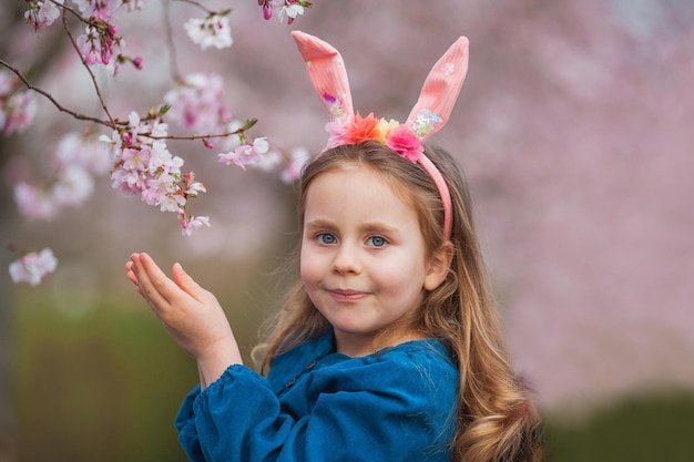 Photo easter little cute girl with long curly hair with bunny ears in cherry blossoms spring holidays